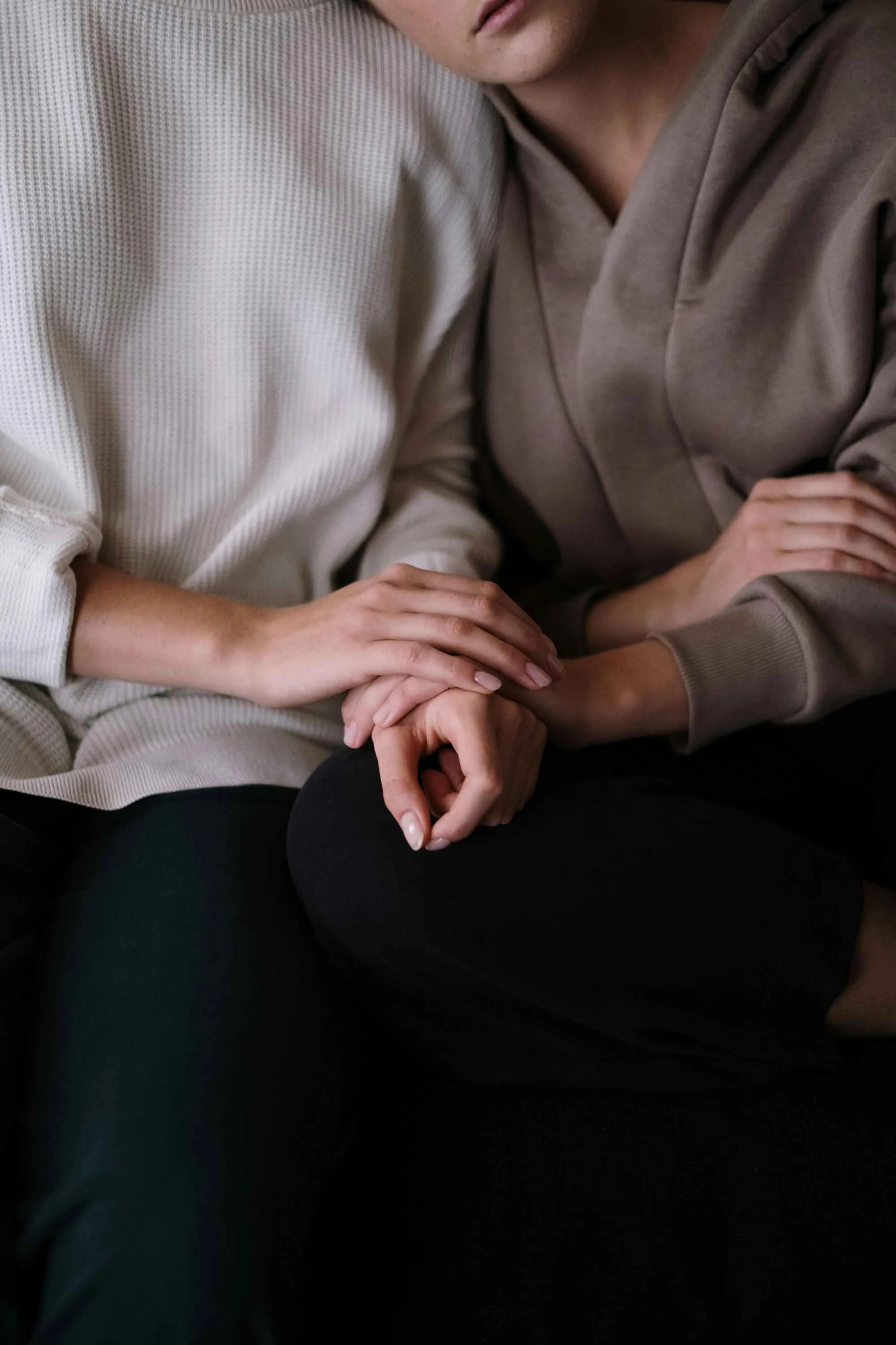 Two people sitting close, one gently holding the other's hand on their lap.