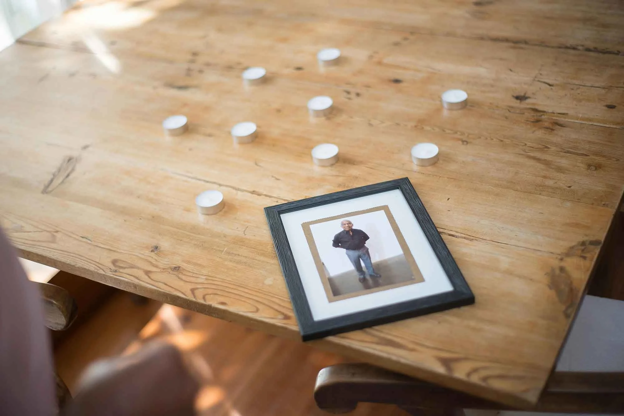 A wooden table with a framed photograph of an older man wearing glasses and tealight candles.