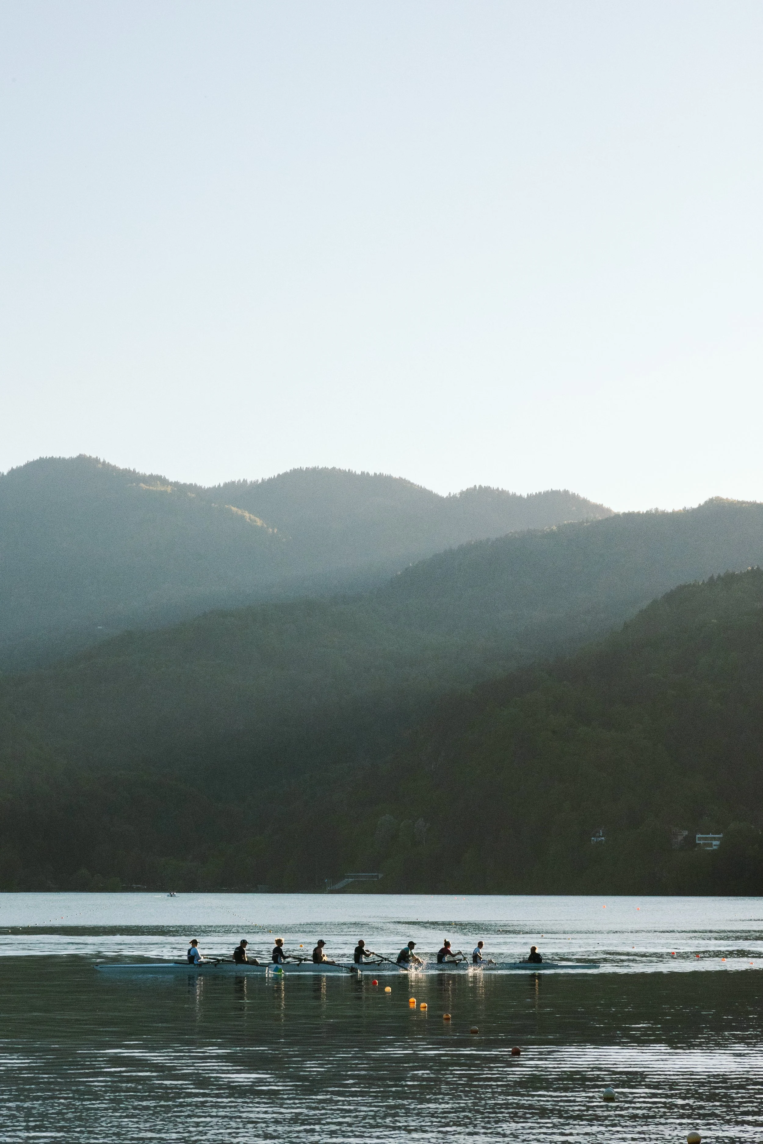 Menschen beim Rudern auf einem See mit Bergen im Hintergrund, am Tag mit ruhigem Wasser.