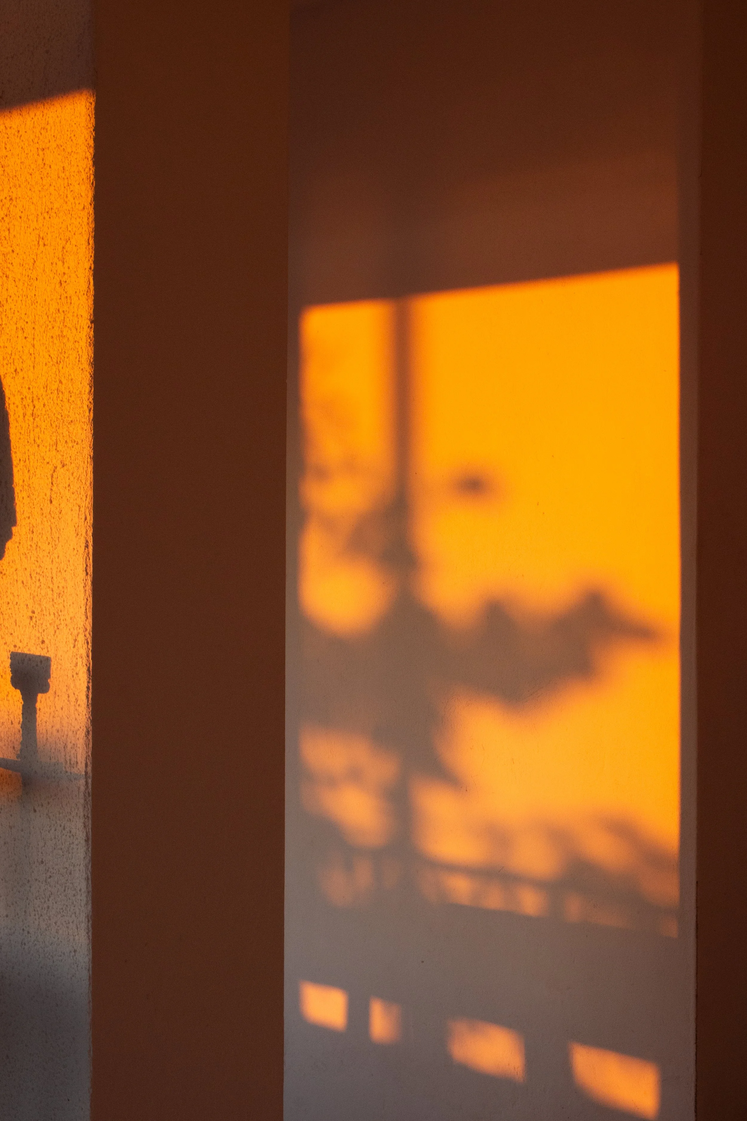 Schatten von Fensterläden auf eine helle Wand bei Sonnenuntergang.