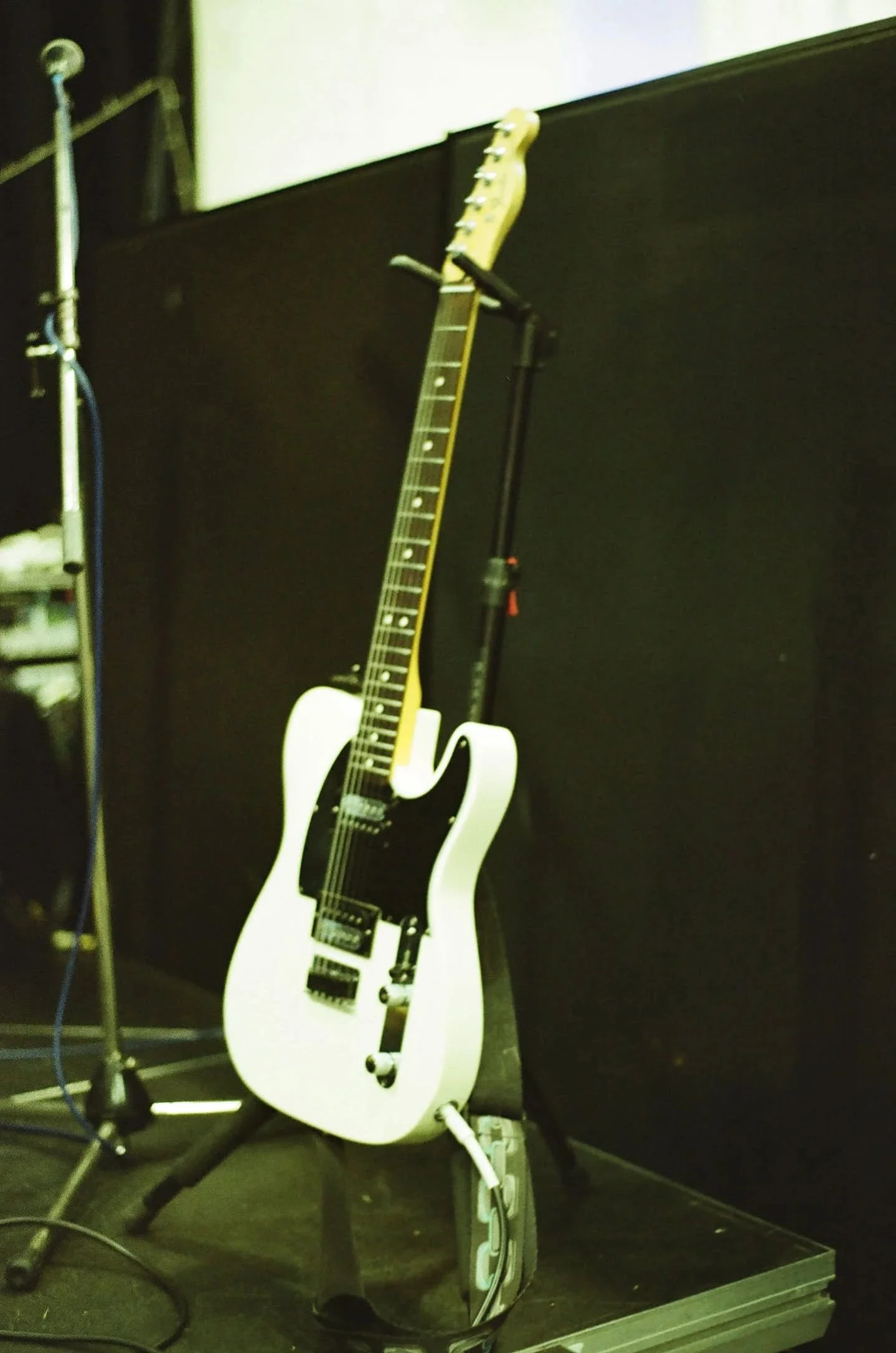 White electric guitar on a stand in a music rehearsal space, surrounded by microphones and equipment.