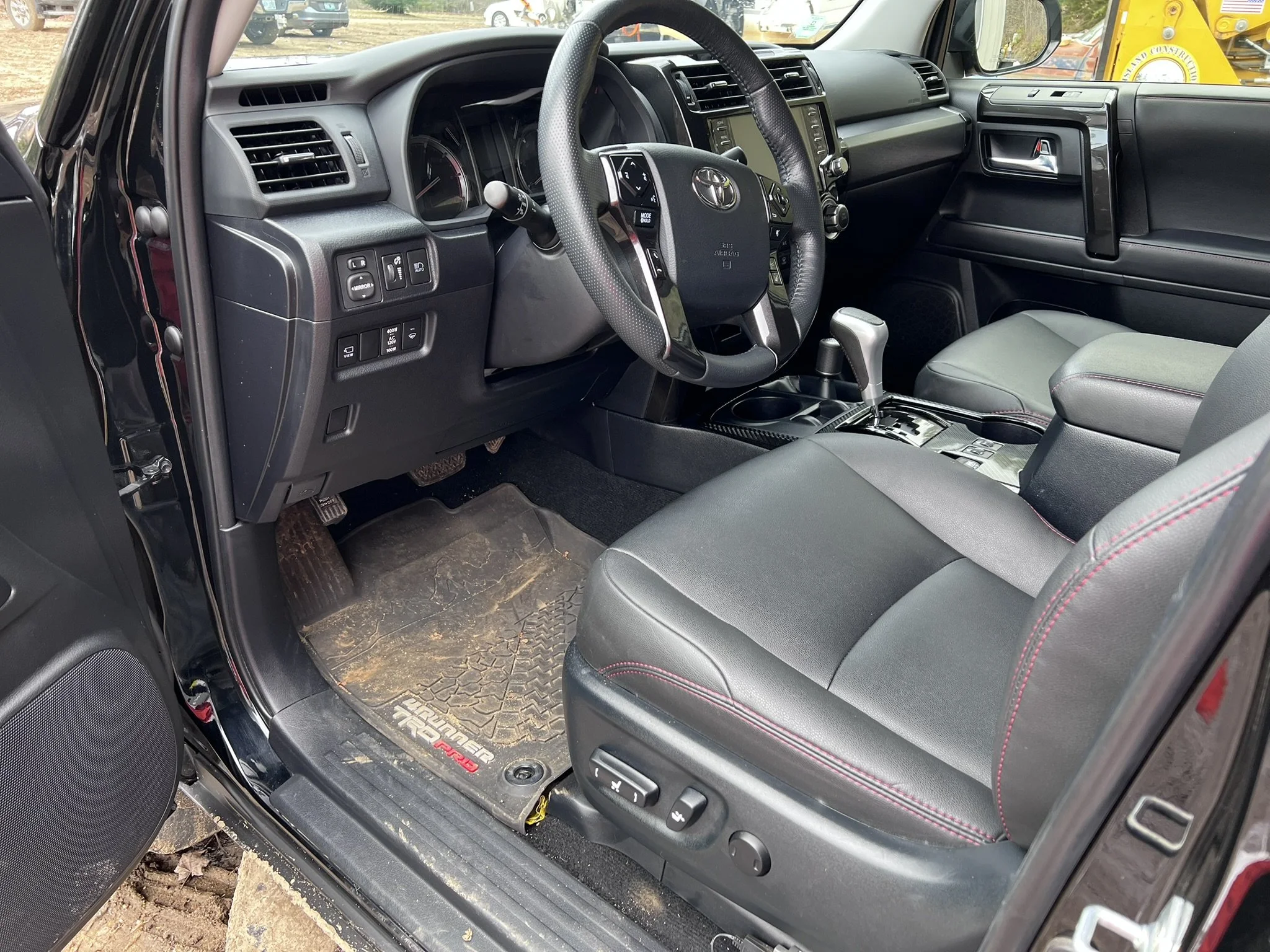 Interior of a black Toyota vehicle showing the driver's seat, steering wheel, dashboard, gear shift, and floor mat with some dirt and mud.