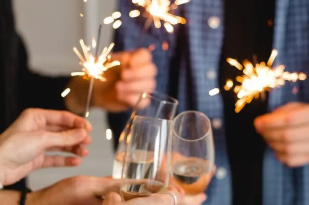 People celebrating with sparklers and glasses of champagne or sparkling wine.