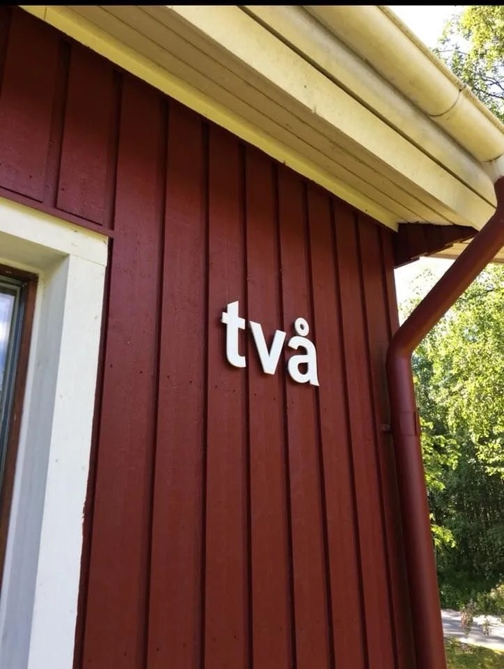 Husnummer 'två' i vit akryl på röd träfasad – svenska villa