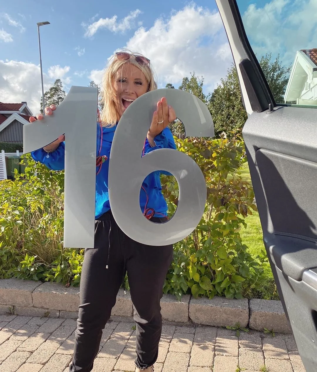 Kvinna håller husnummer 16 i vit akryl – stor fasadsiffra utomhus