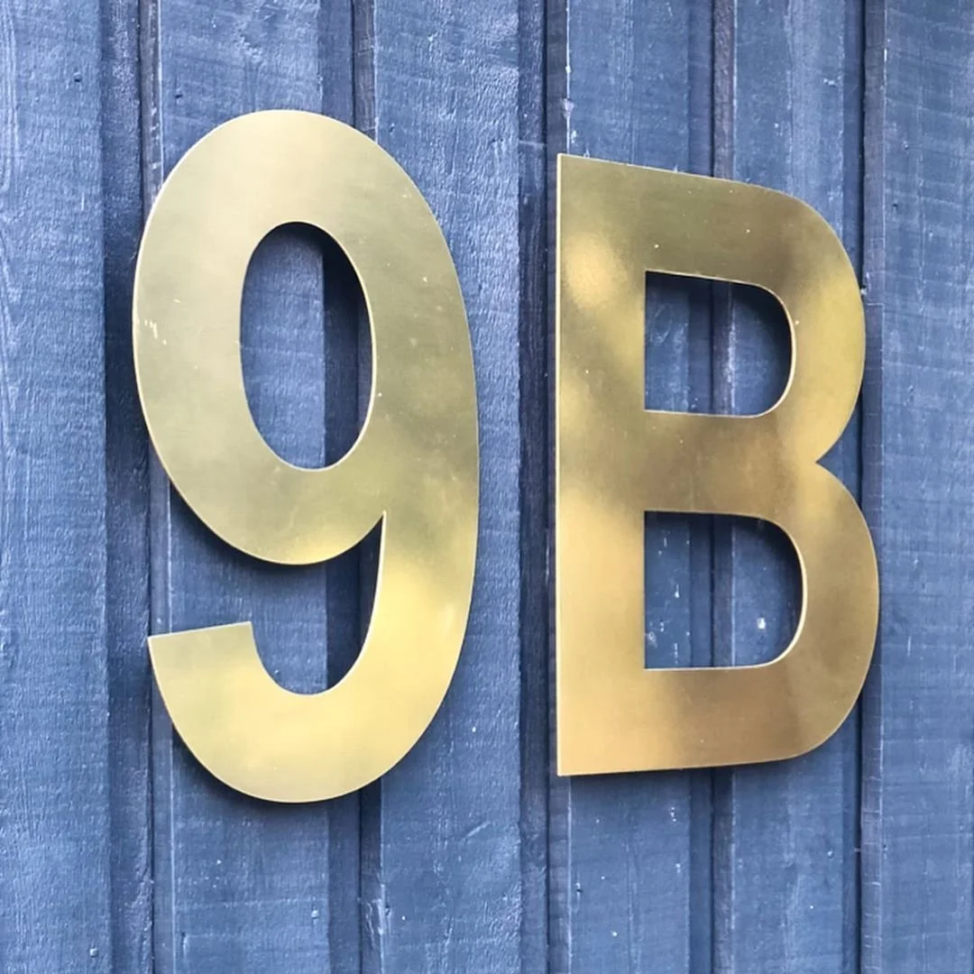Husnummer 9B i guld/mässing på mörkblå träpanelfasad