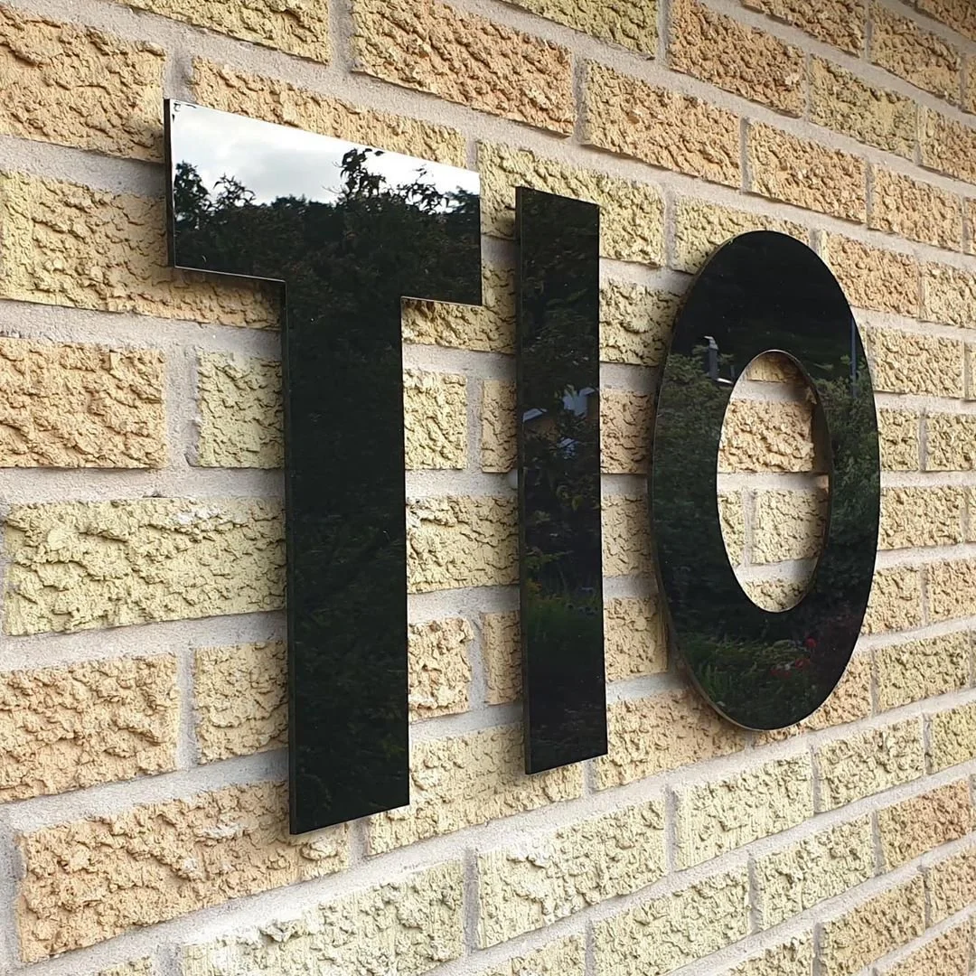 Fasadtext 'TIO' i svart akryl på sandstensvägg – hus med karaktär