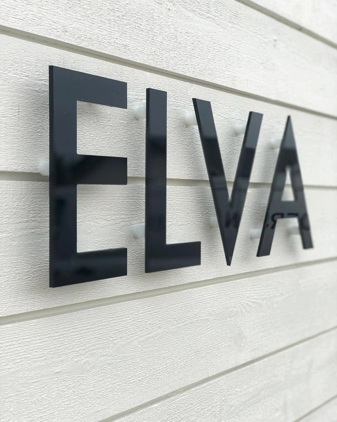 Fasadtext 'ELVA' i svart stål på vertikal träpanel – modern villa