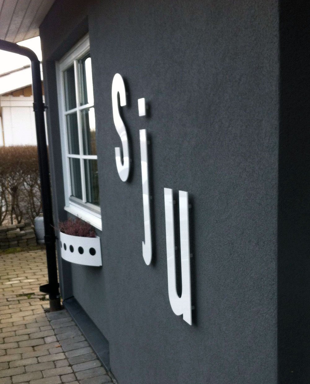 Fasadtext 'sju' i stål med fönster på svart fasad – kreativ adressmarkering