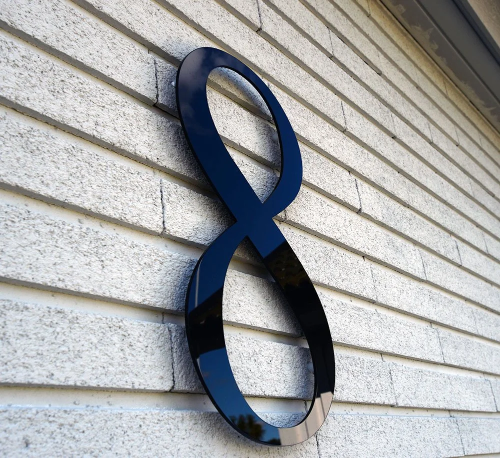 Husnummer 8 i svart akryl på vit horisontell träpanelfasad