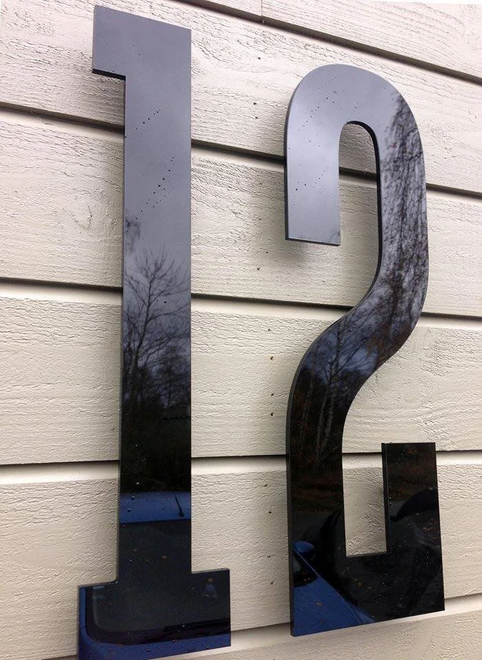 Husnummer 12 i svart akryl på vit horisontell träpanelfasad