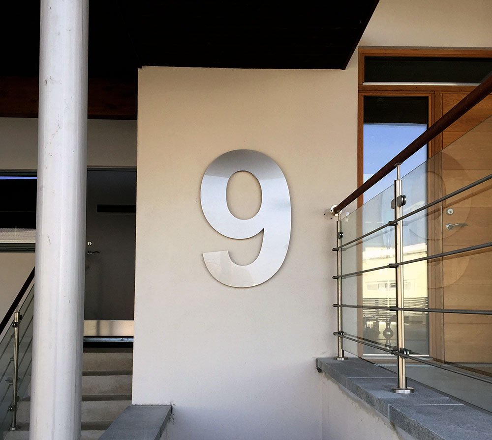 Husnummer 9 i borstat stål på cremevit putsad husvägg