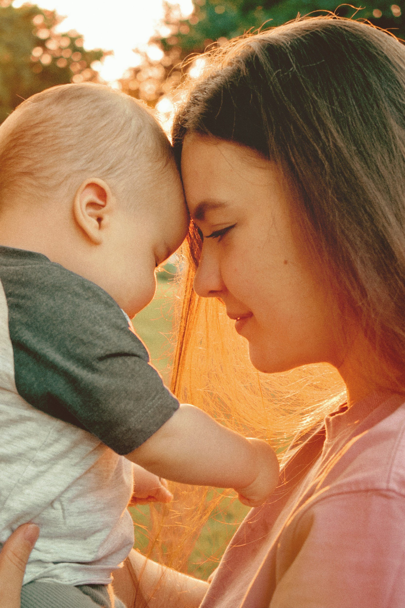 mum and baby in nature touching foreheads with pale orange light