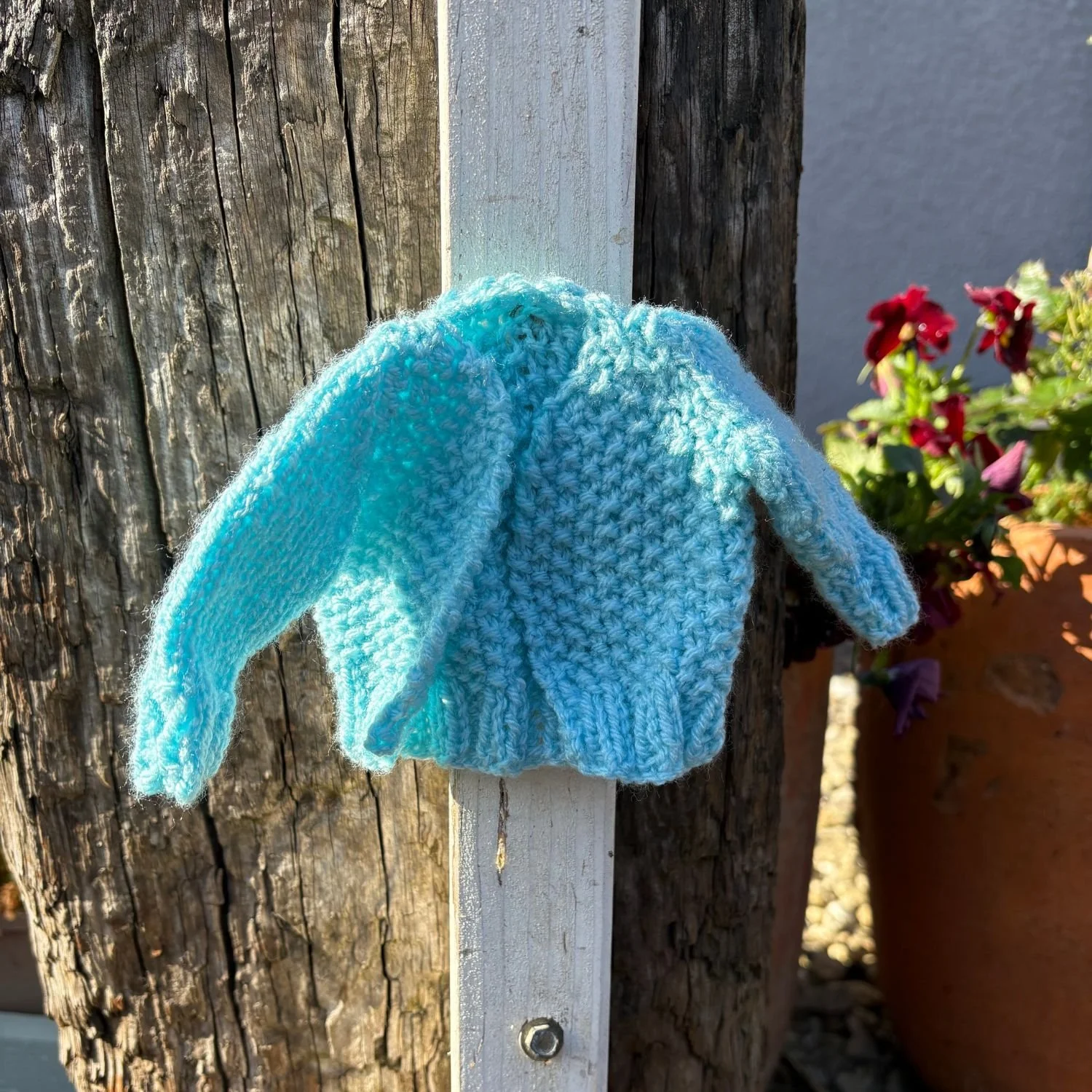 Tiny baby blue knitted cardigan hanging on a white post outdoors in spring light for Ranks of Women campaign yarn bomb for life