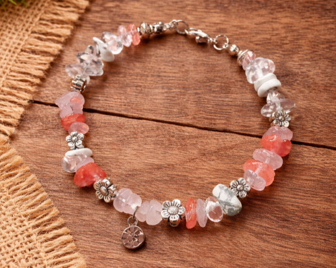 Beaded bracelet with pink, clear, and white stones and silver flower charms on a wooden surface.
