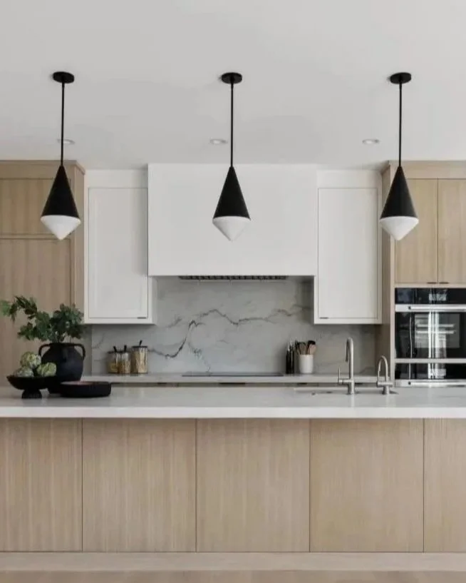 Modern kitchen with white cabinets, marble backsplash, wooden lower cabinets, and black pendant lights.