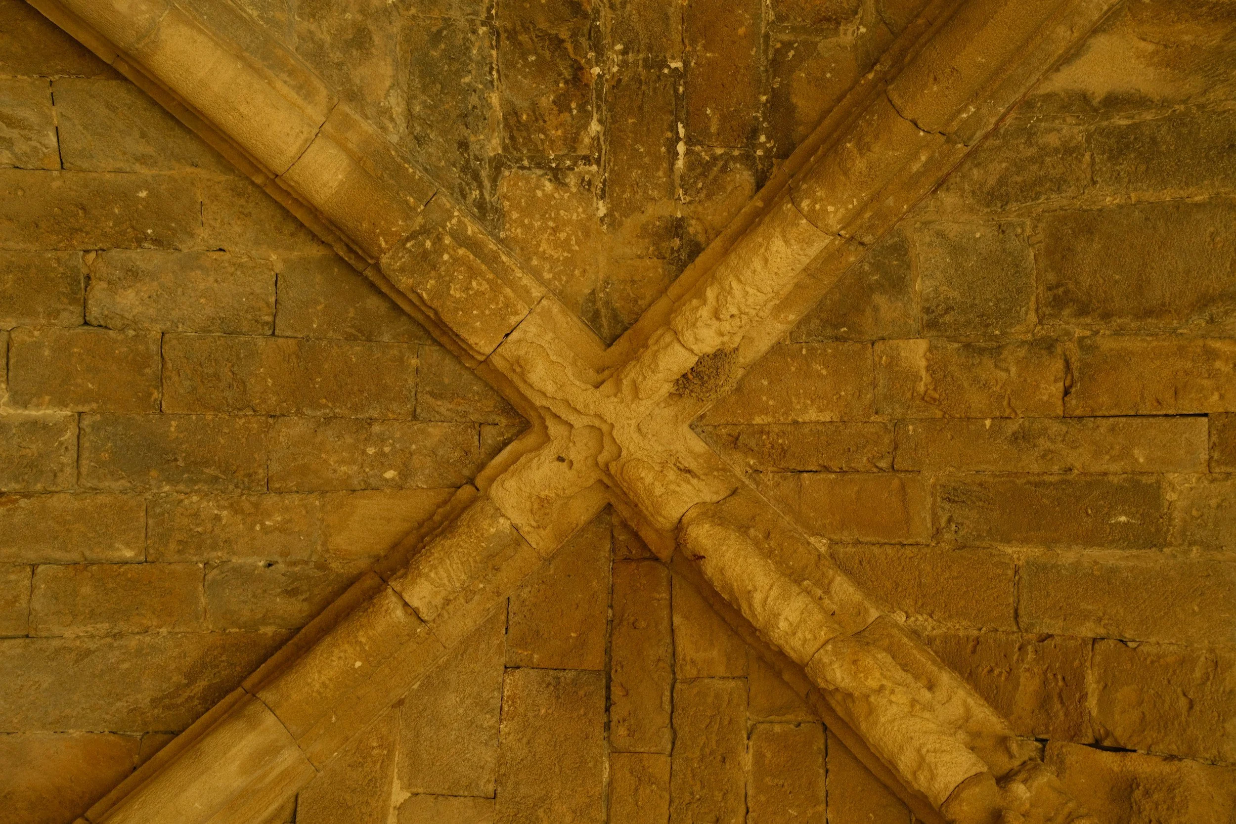 Close-up of Gothic stone ceiling with ribbed vaults and pointed arches, constructed from large rectangular stones forming a crossroads