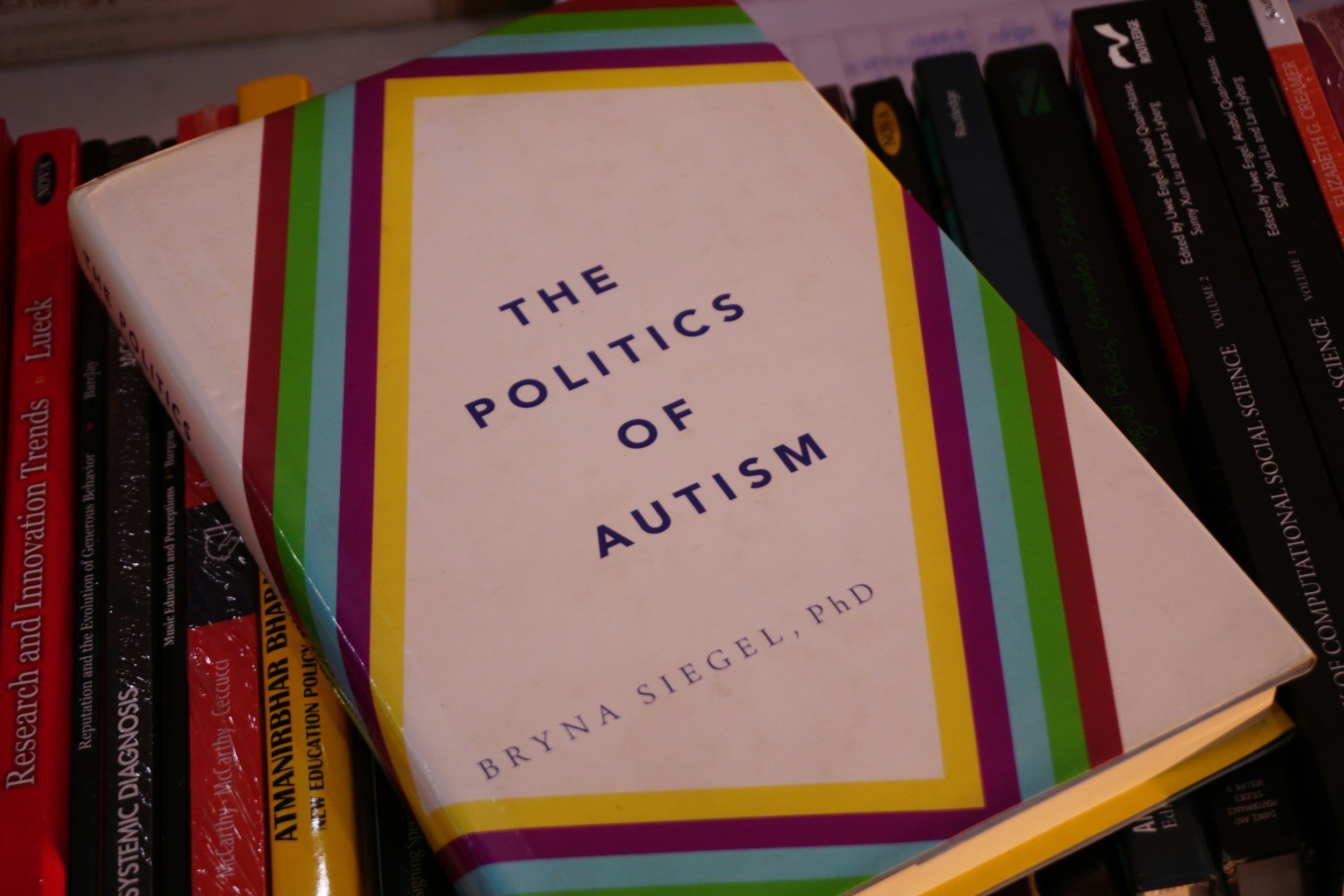 A book titled 'The Politics of Autism' by Bryna Siegel PhD on a shelf among other books.