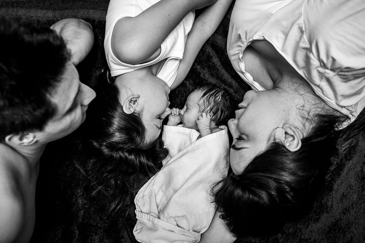 black and white candid portrait of family on on the floor watching baby sleep