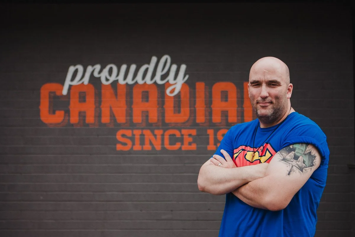Standing with arms folded in front of Proudly Canadian since in the background