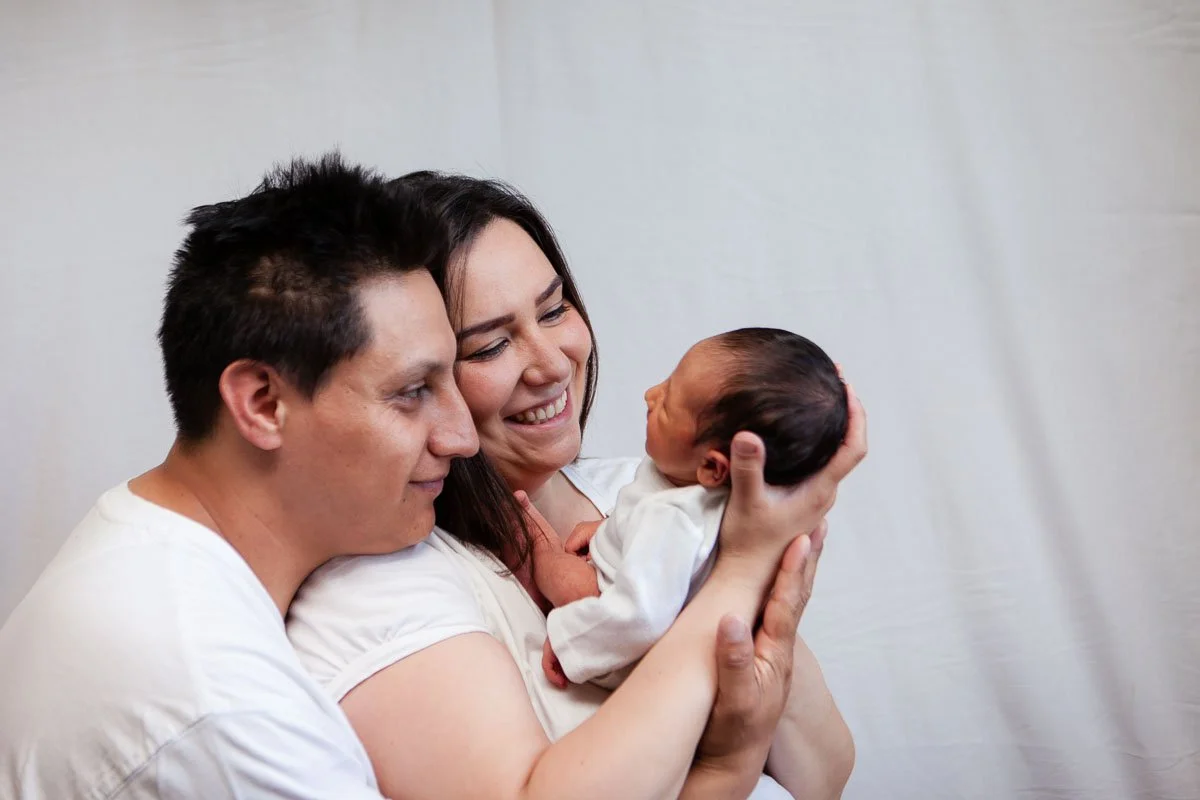 Father hugging mom who is holding baby with a beautiful smile and baby smiling back