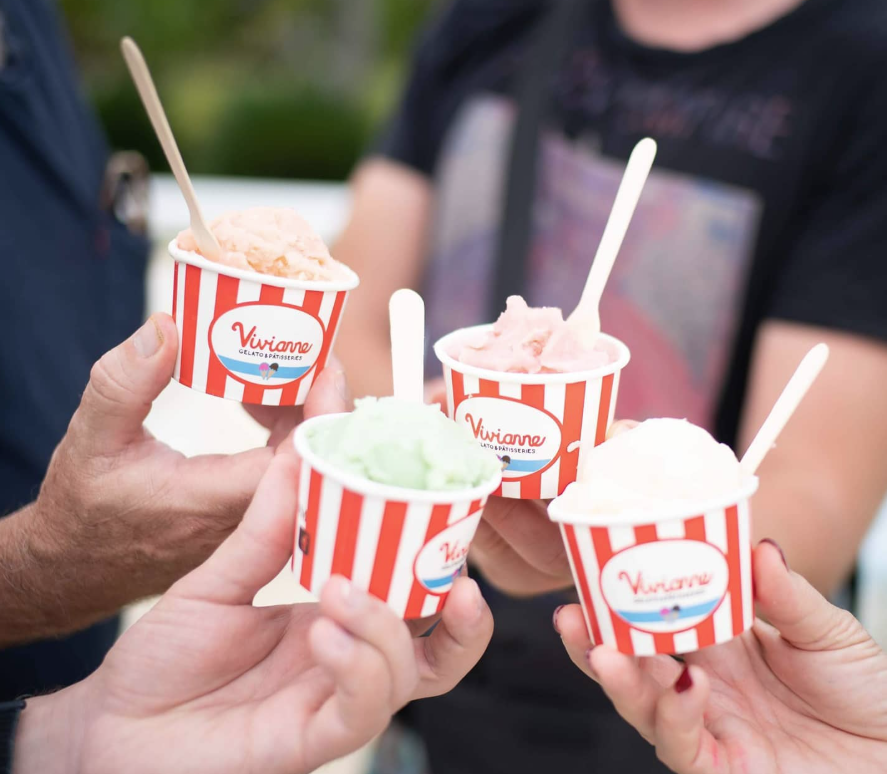 Four people holding cups of colorful gelato ice cream outdoors, each cup with red and white stripes and a Vivianne brand label.