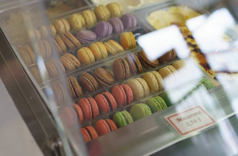 A display case with rows of colorful macarons in various flavors, labeled as 'Macarons 2.50' each.