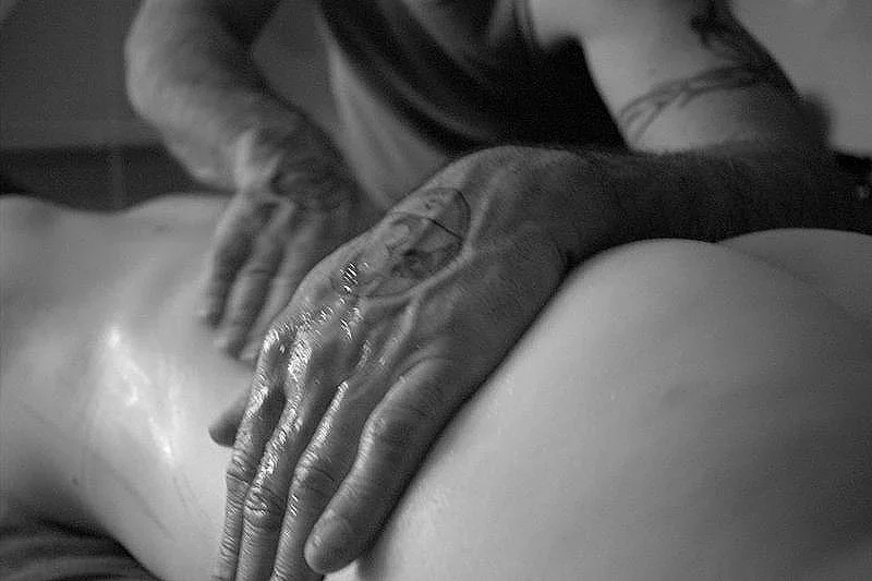 Close-up of a person's hands giving a massage to another person's naked back in black and white.