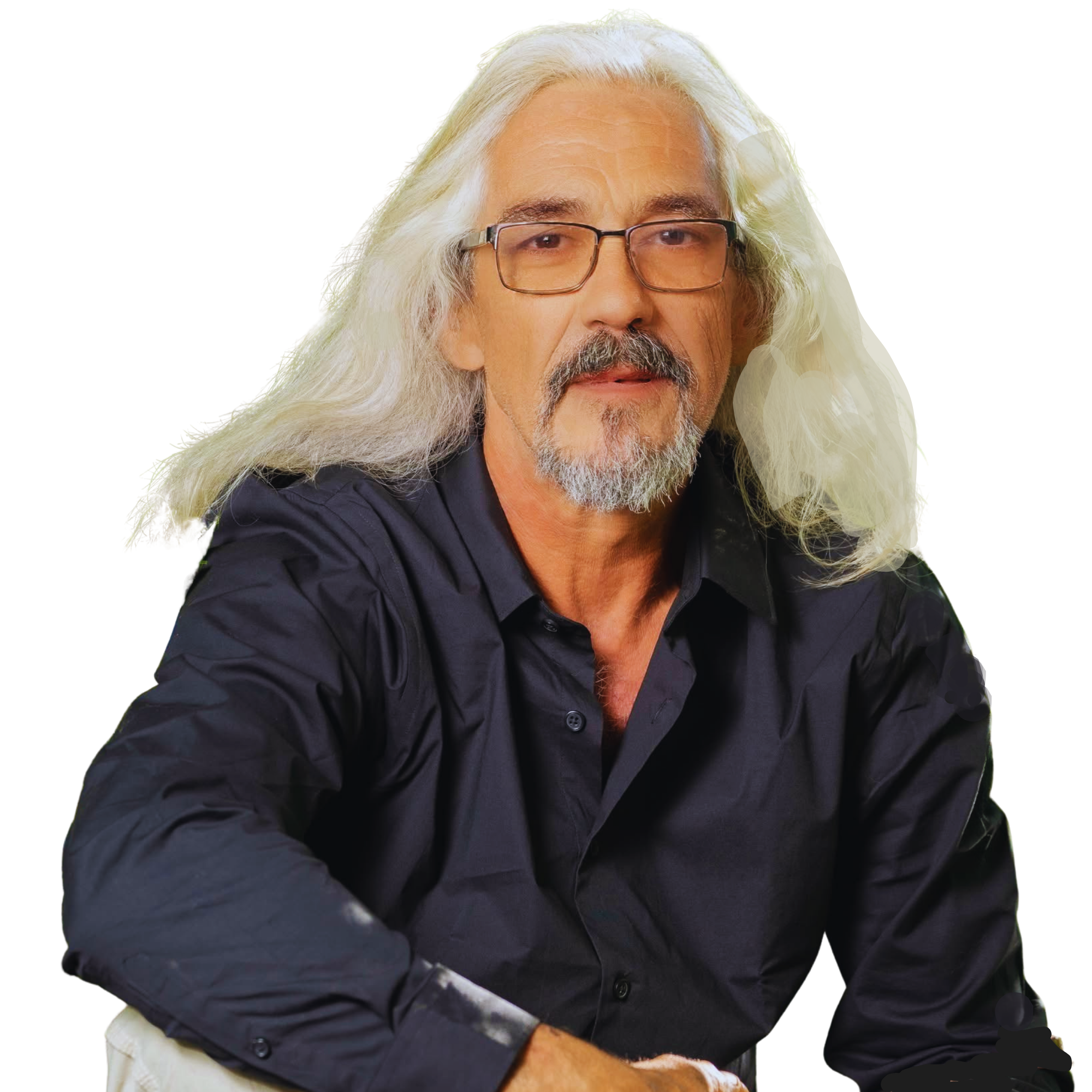 A middle-aged man with long gray hair, a gray beard, and glasses, wearing a black shirt, sitting with his arms resting on a surface, looking at the camera.