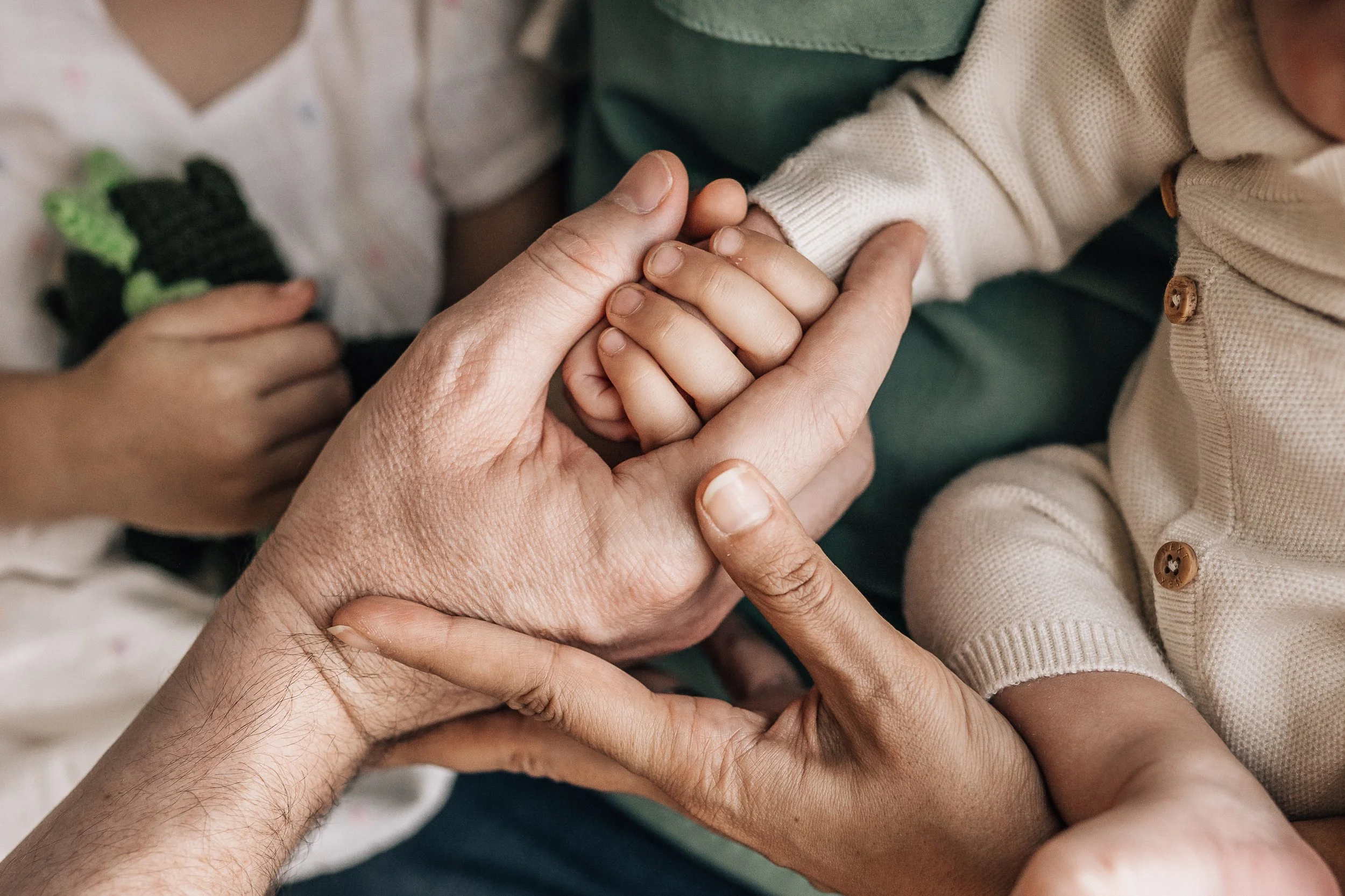 Close-up image of multiple hands gently holding and supporting a child's hand, emphasizing care, connection, and affection.