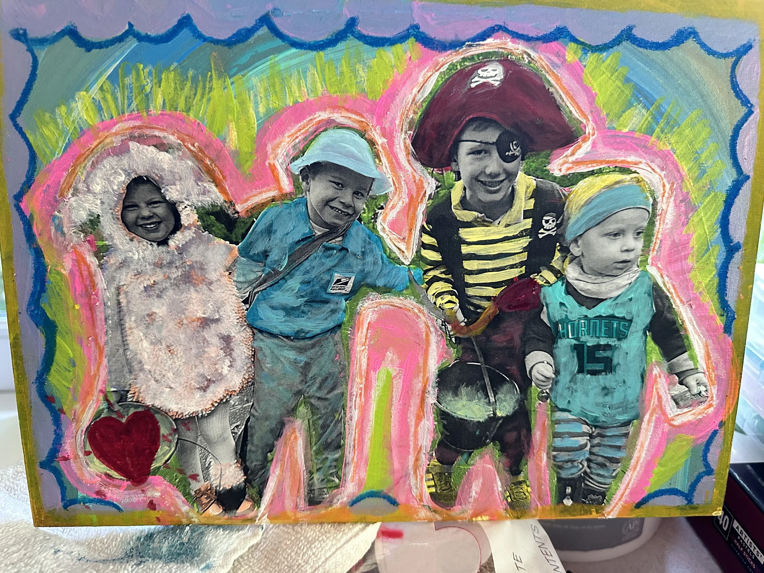A mixed-media artwork featuring a collage of four children with painted, colorful outlines surrounding their black and white photographs. The children are dressed in playful costumes, with bright colors, pirate, sports, and casual attire. The background of the collage includes vibrant, abstract colors and patterns, with some painted elements like hearts and a rainbow-like border.