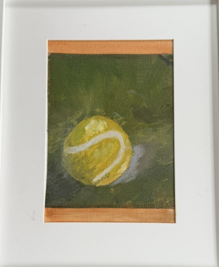A small abstract painting of a yellow tennis ball with white lines on a dark green background, framed with a white mat and a thin gold or orange border.