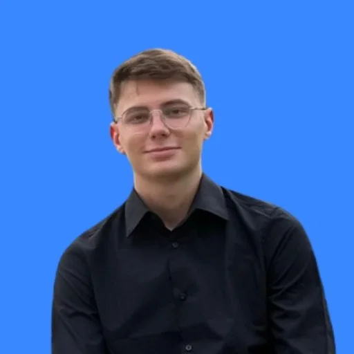 Young man with short hair and glasses wearing a black shirt, smiling against a solid blue background.