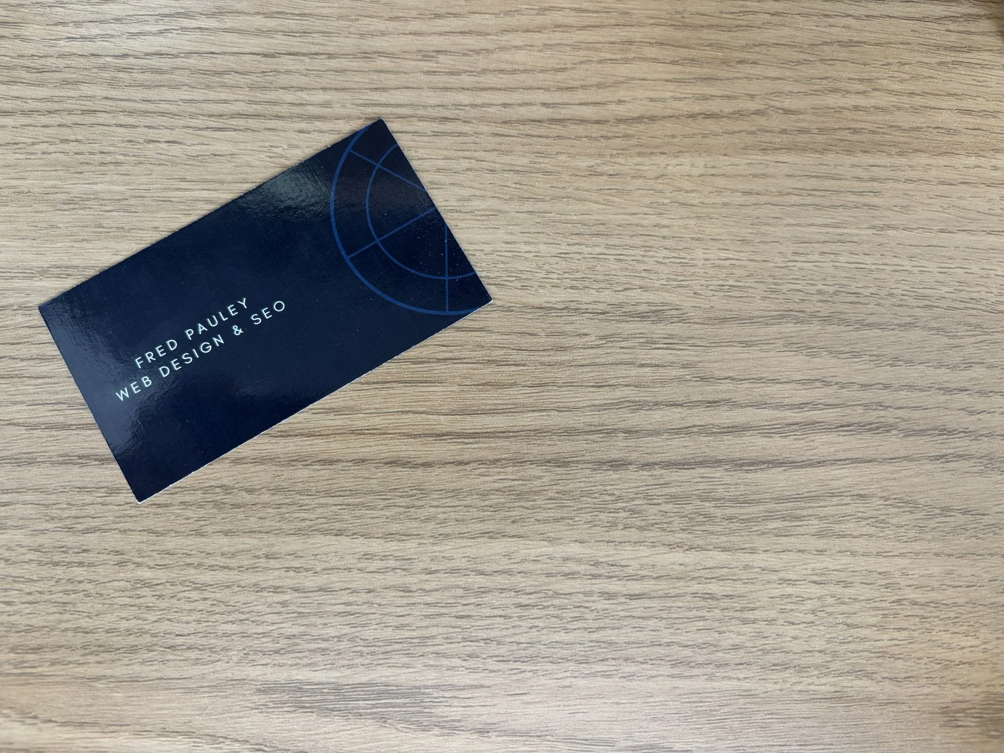 A business card for Fred Pauley, Web Design & SEO, resting on a light wood surface.