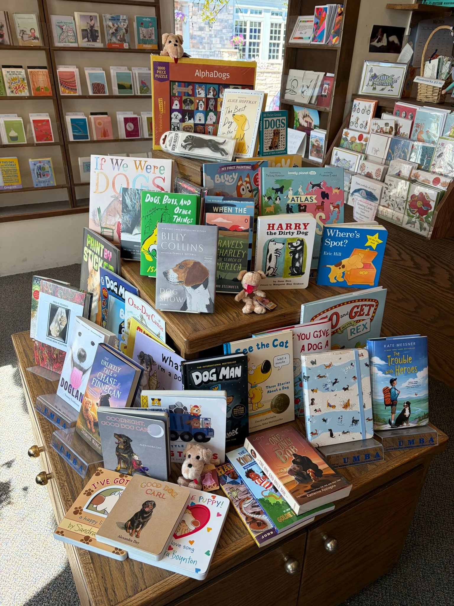 A display of children's books and stuffed dog toys on a wooden table in a bookstore, with books about dogs, flowers, and other topics.