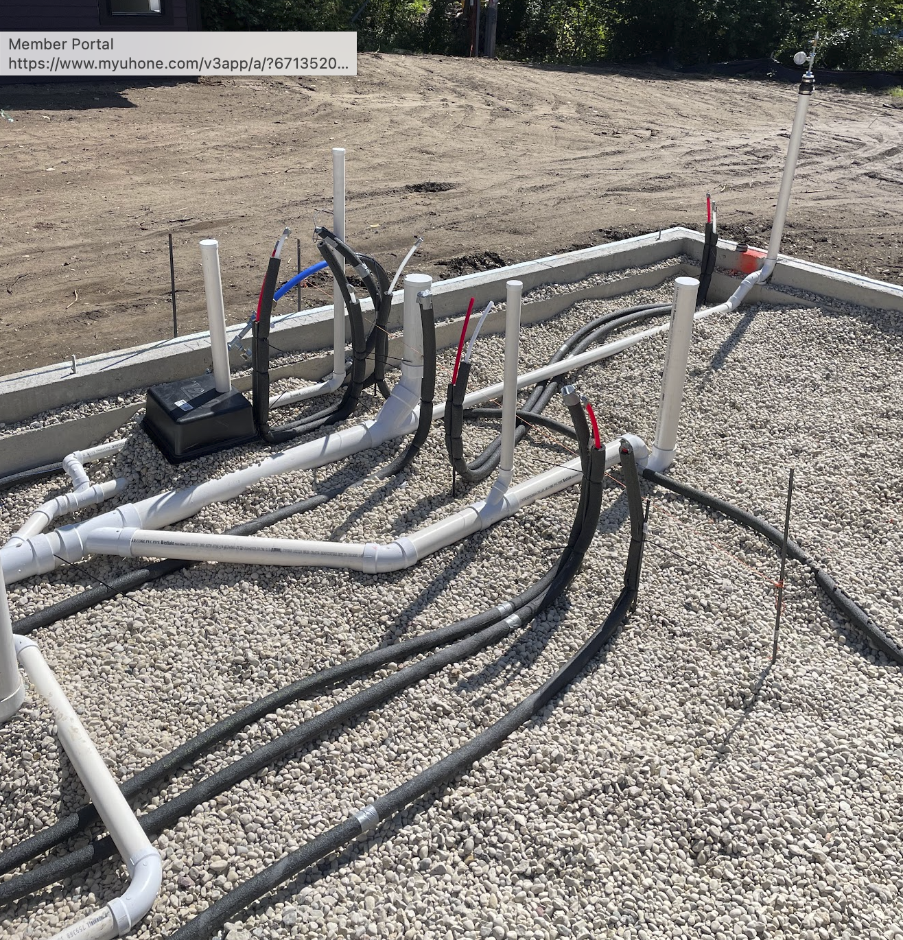 Construction site with plumbing pipes and electrical wiring installed on gravel ground.