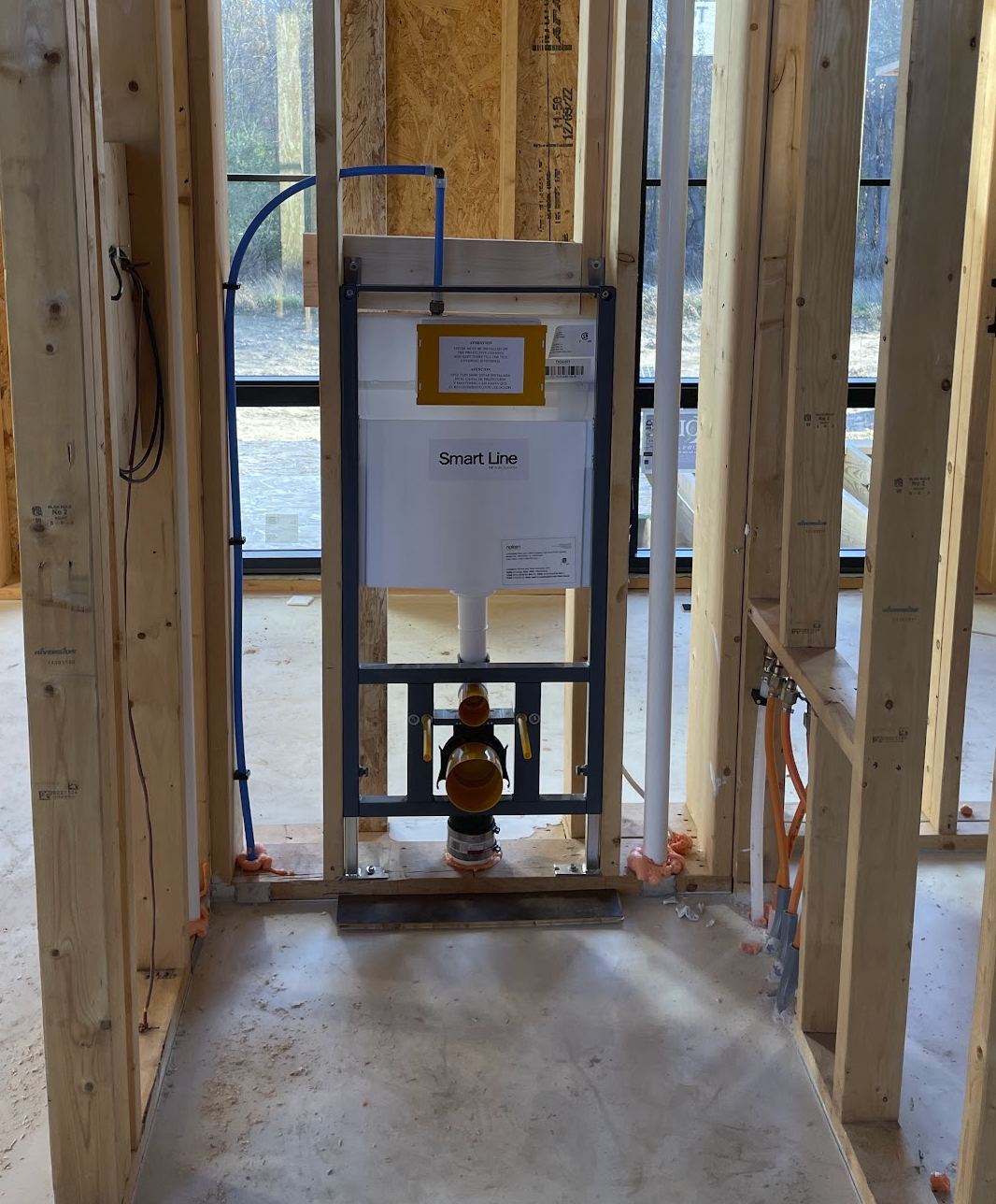 Installation of a Smart Line toilet system inside a house under construction, with exposed wooden framing and large windows in the background.