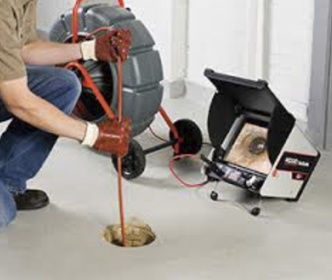 A person using a drain snake machine to clear a clogged drain on a concrete floor.
