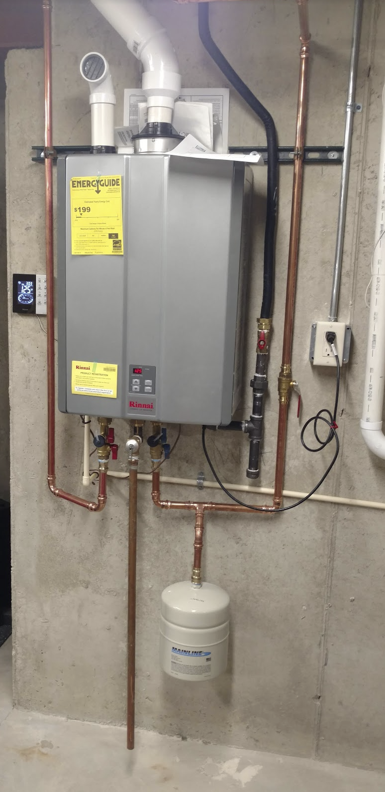 A wall-mounted Rinnai tankless water heater system installed with copper piping, an expansion tank, and a digital display, in a utility room.