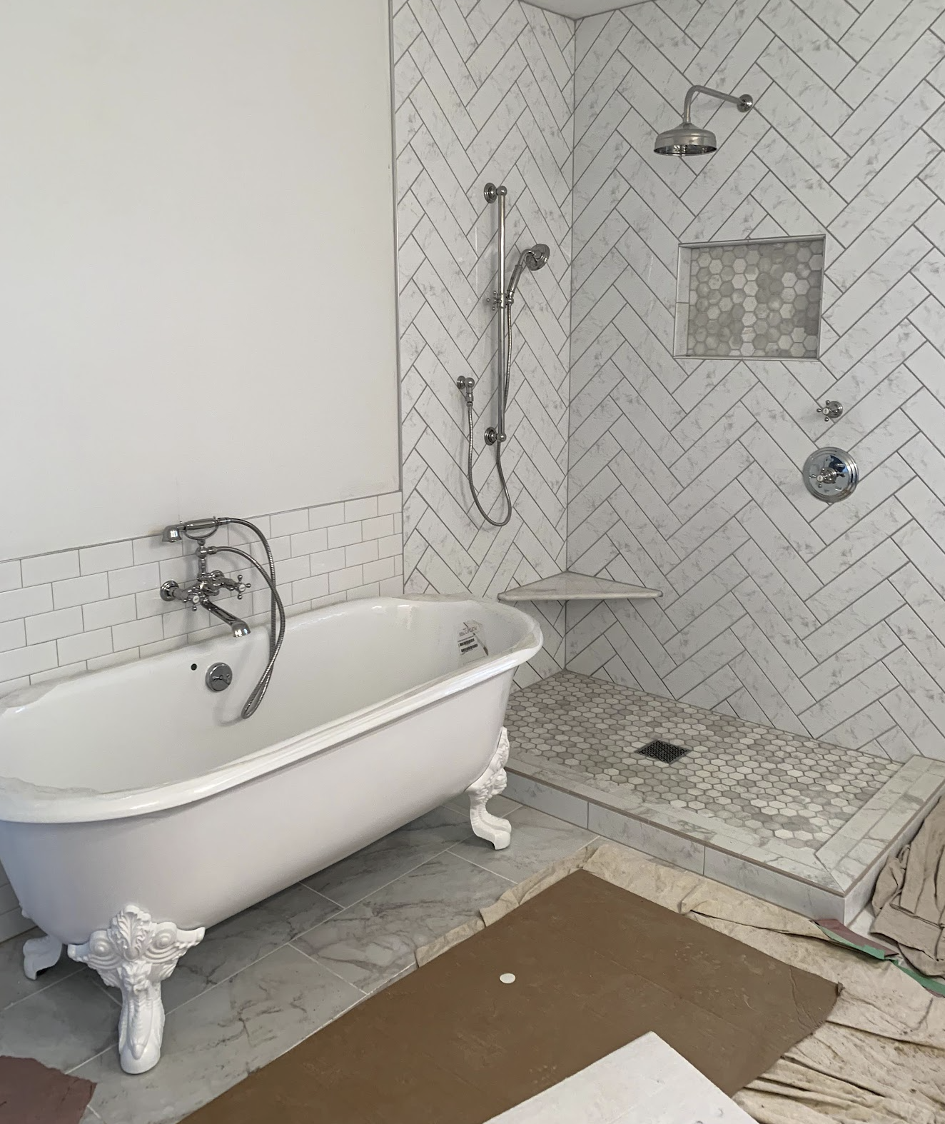Bathroom with a vintage clawfoot bathtub, a walk-in shower with marble tile walls in a herringbone pattern, a small built-in shower niche, and marble flooring.