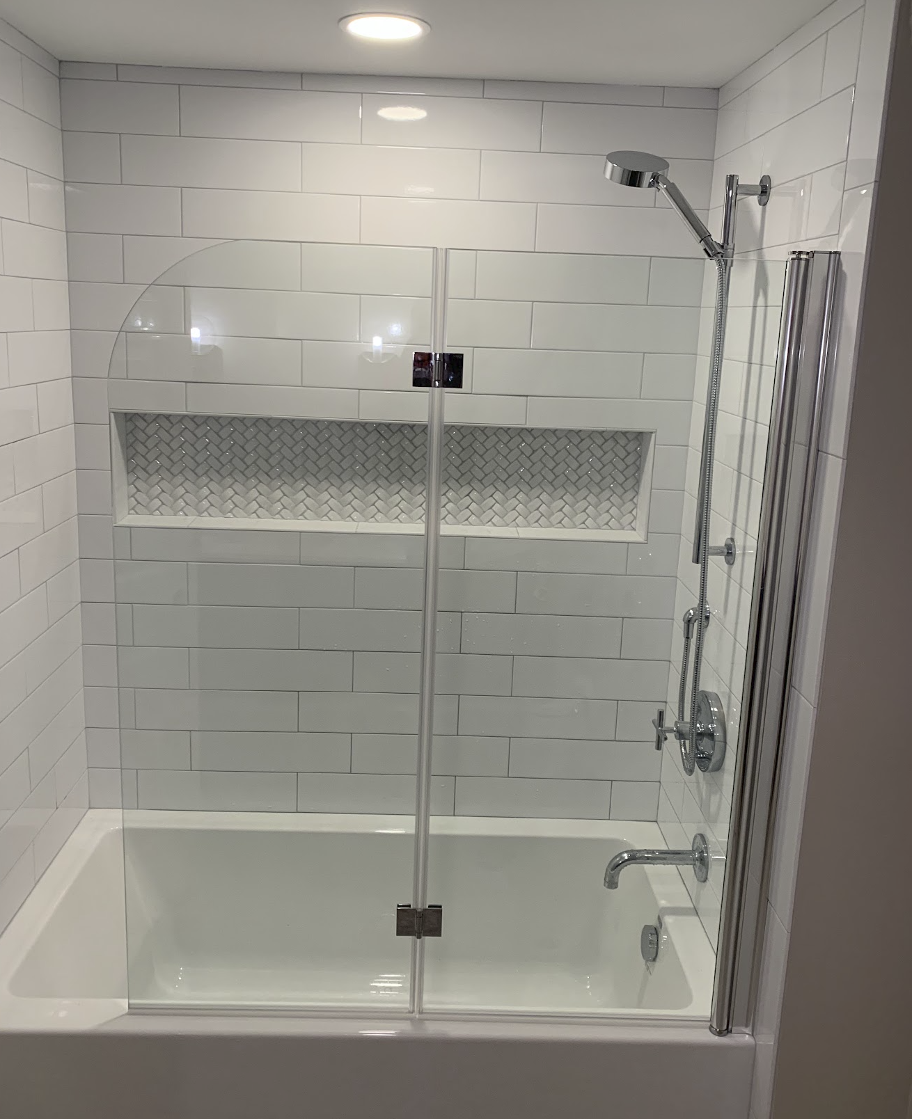 Bathroom shower with white subway tile walls, a woven tile accent niche, a glass door, and a chrome showerhead.