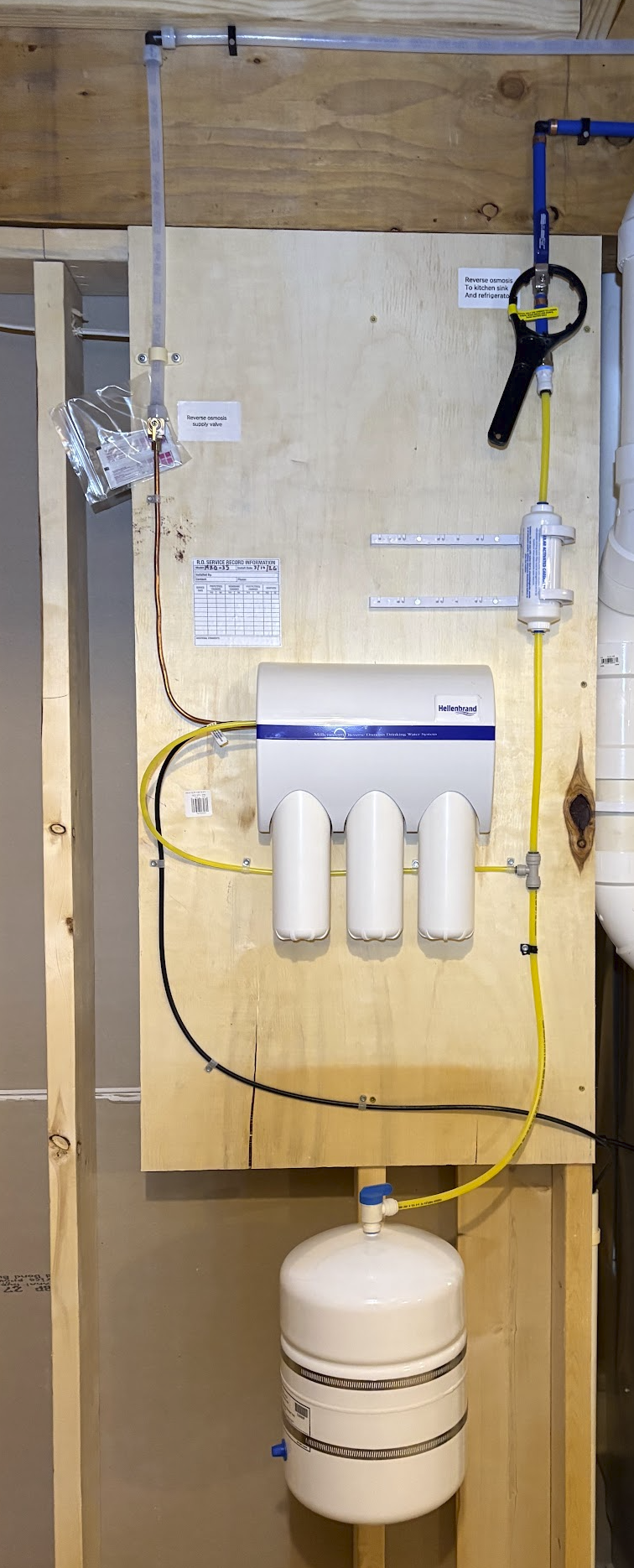 Water filtration system with reverse osmosis components attached to a wooden wall, including tubes, gauges, and filters.