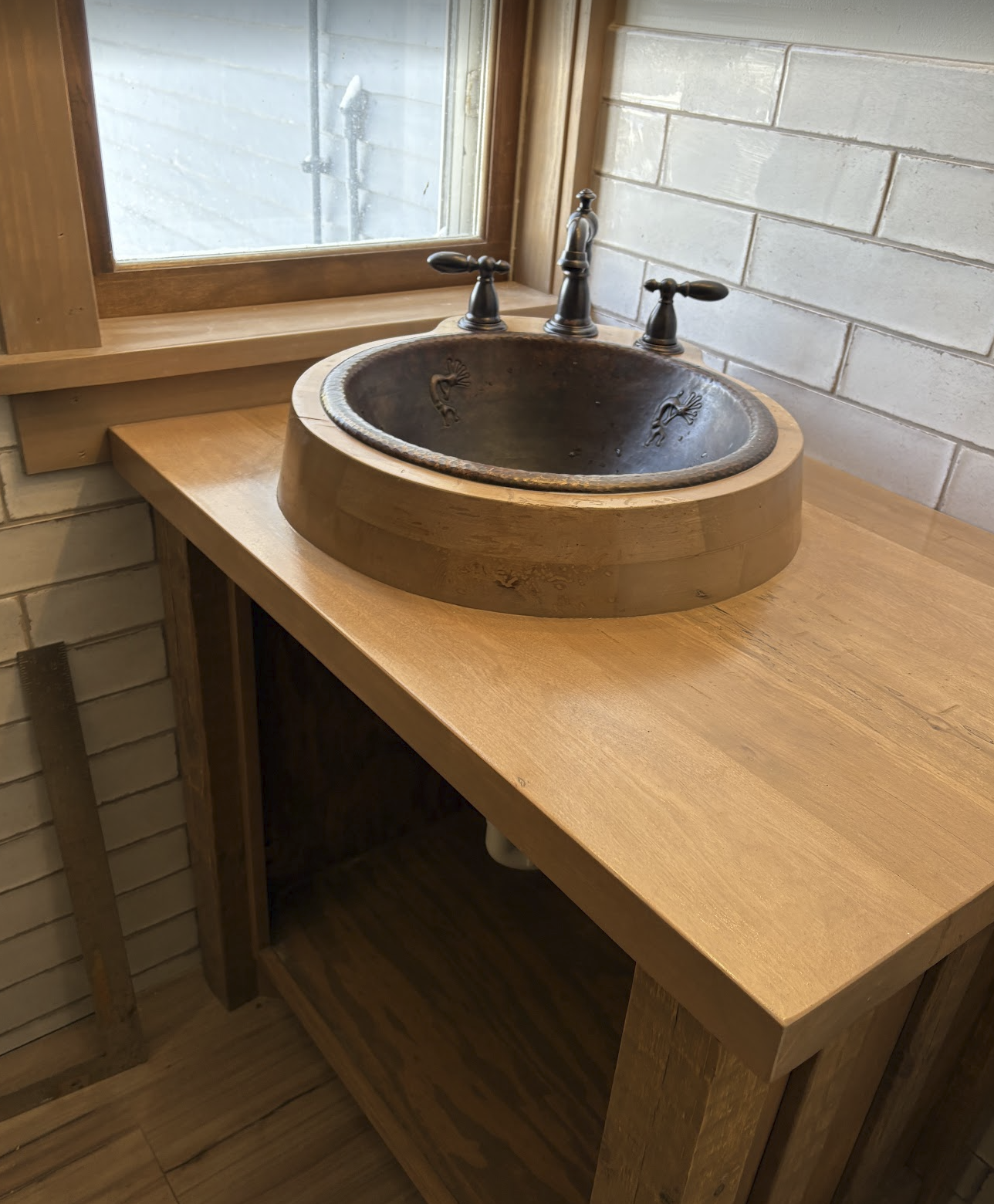 Wooden bathroom vanity with a stone bowl sink and bronze-colored faucet next to a window