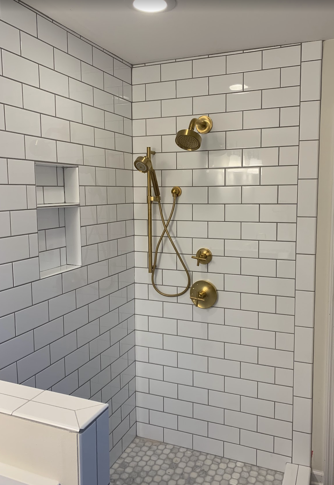 A modern shower with white subway tile walls, gold fixtures, and a built-in niche for toiletries.