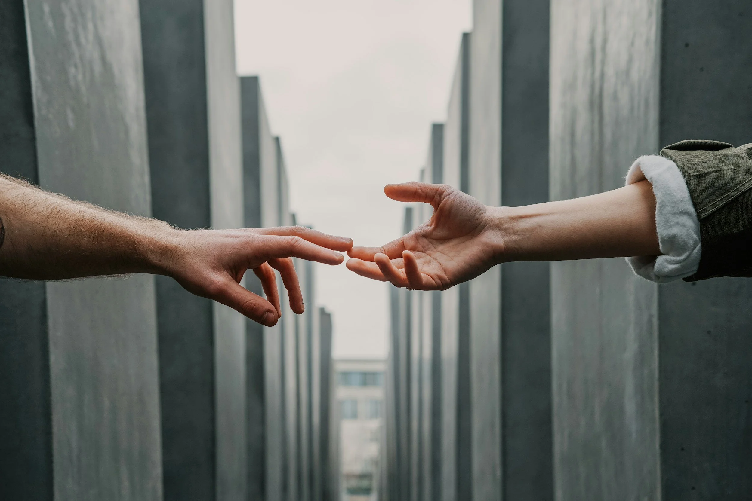 Two hands reaching towards each other in front of a modern architectural background.