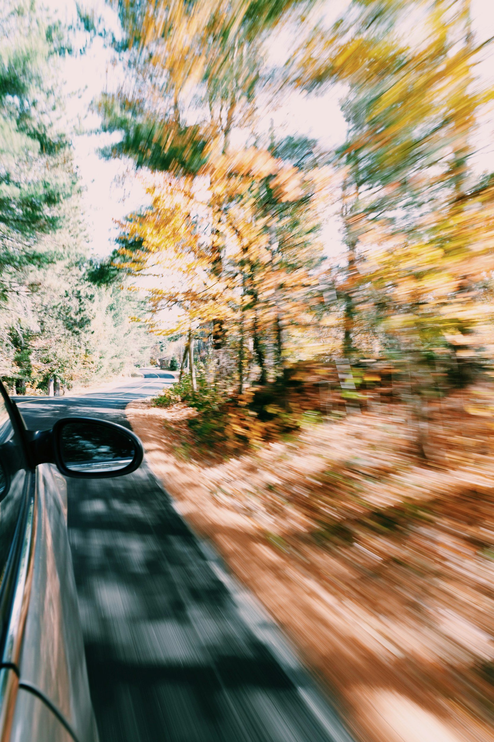A car driving on a winding road through a forest with autumn-colored leaves, captured with motion blur.