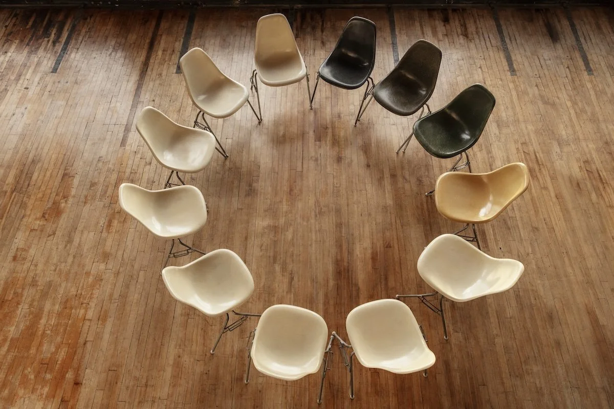 A circle of chairs on a wooden floor, with a mix of beige, black, and brown chairs arranged in a wide semi-circle. Addison Leadership Advisory, Dr. Asha Gipson