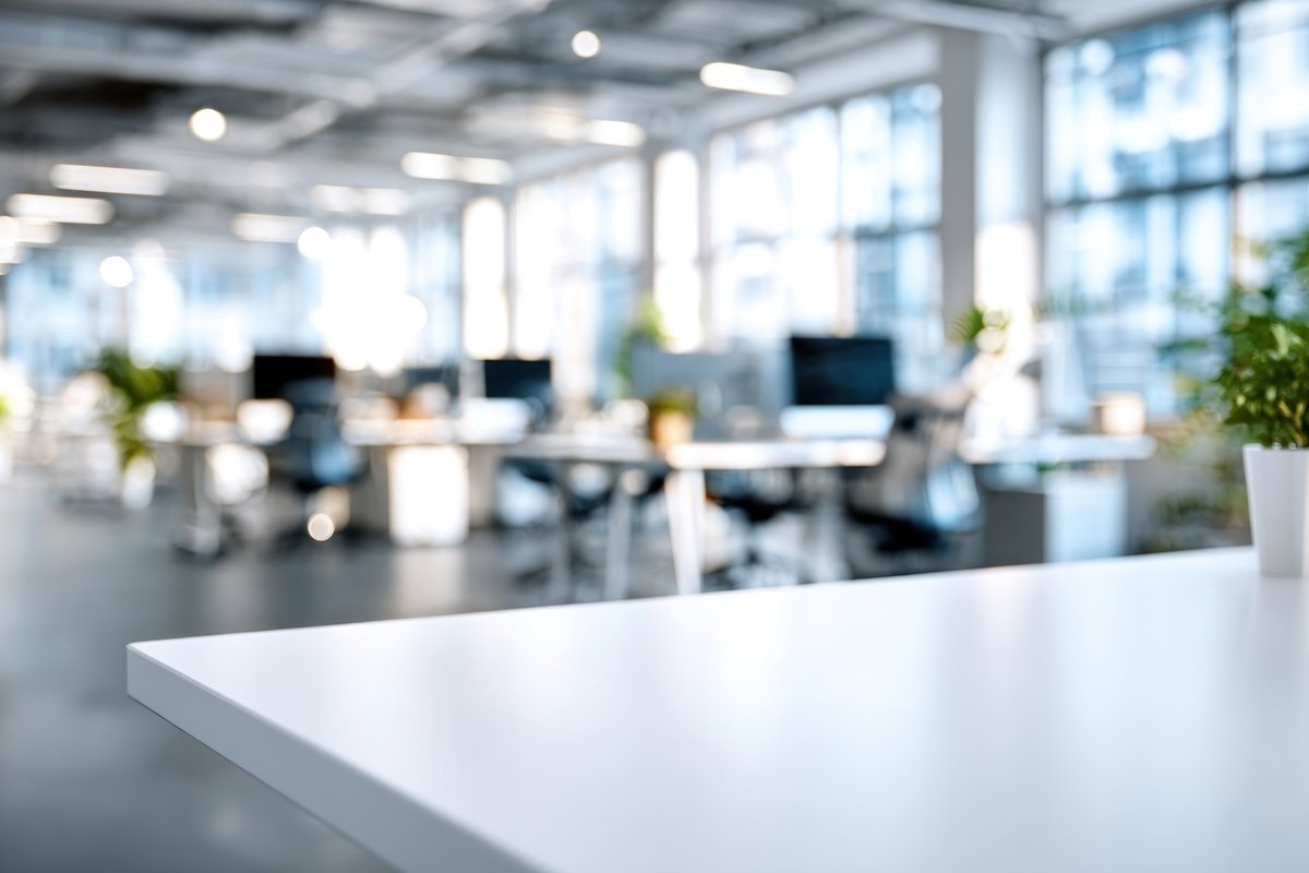Blank white table in an open office with desks, chairs, and large windows in the background. Addison Leadership Advisory, Dr. Asha Gipson