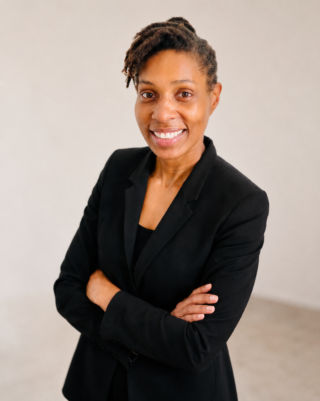 Dr. Asha Gipson with natural hairstyle smiling at the camera, wearing a black blazer with arms crossed against a plain light background.  Addison Leadership Advisory