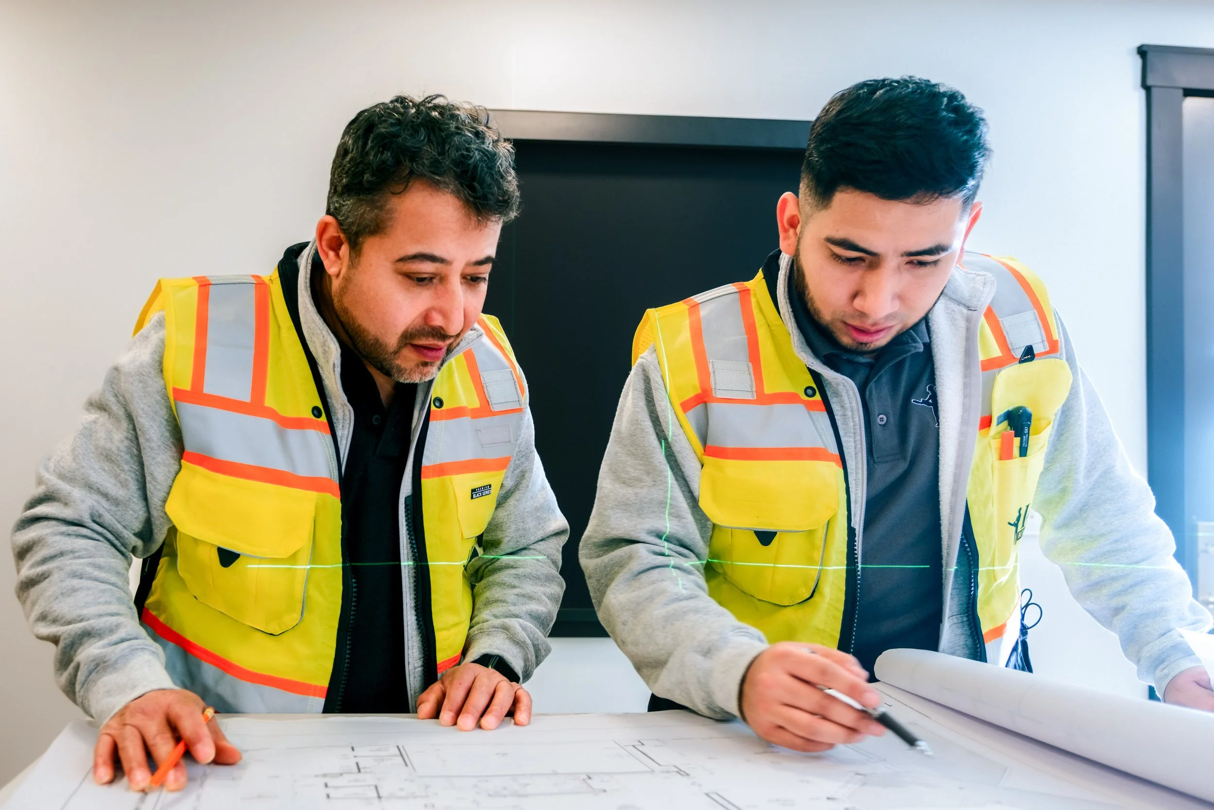 Two men in safety vests examining architectural plans at a table.